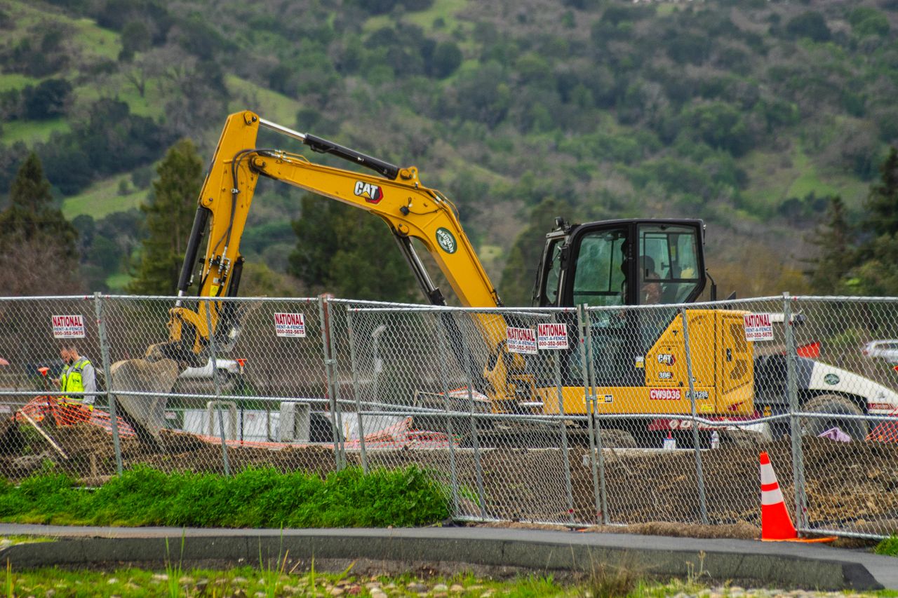 A yellow excavator and earthmoving work area behind a temporary fence.