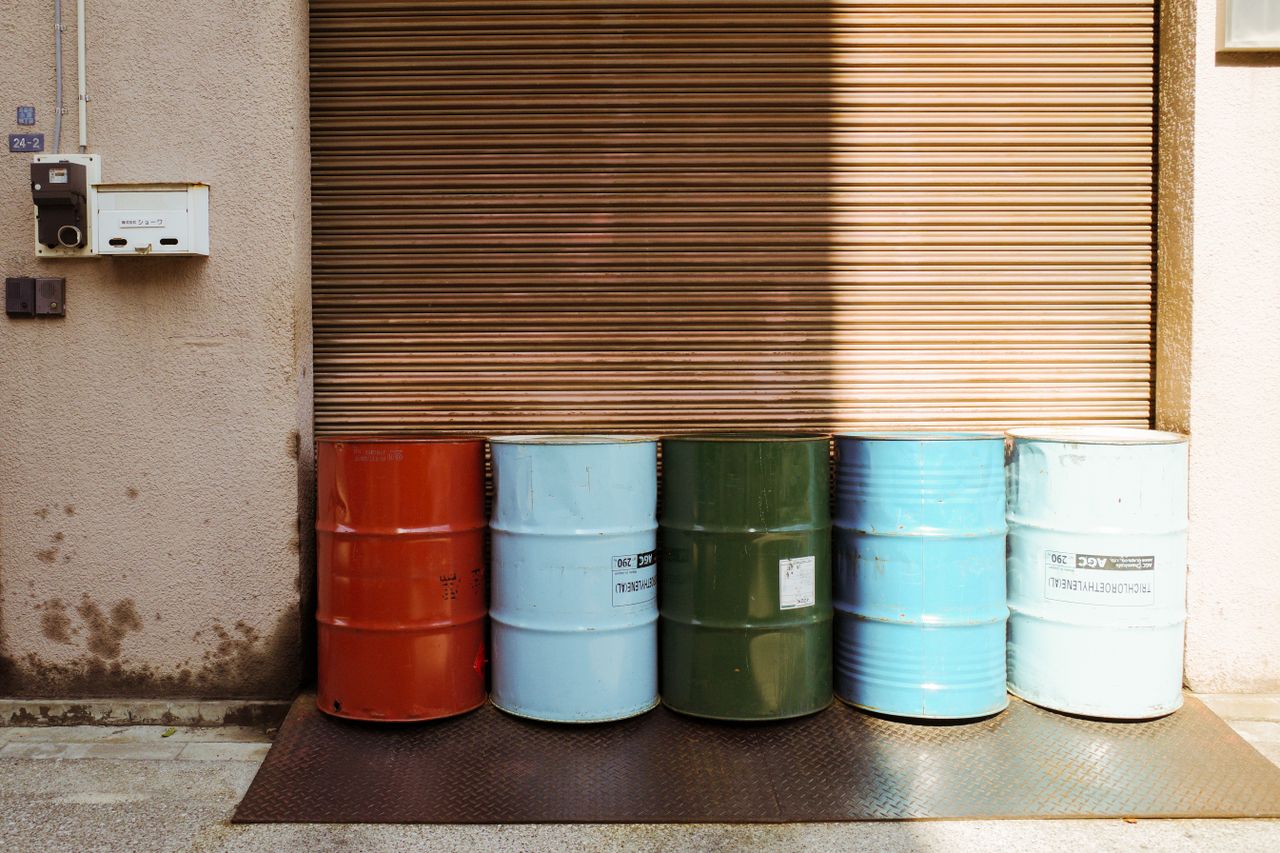 Five steel drums of different colors standing in front of a closed roller door.